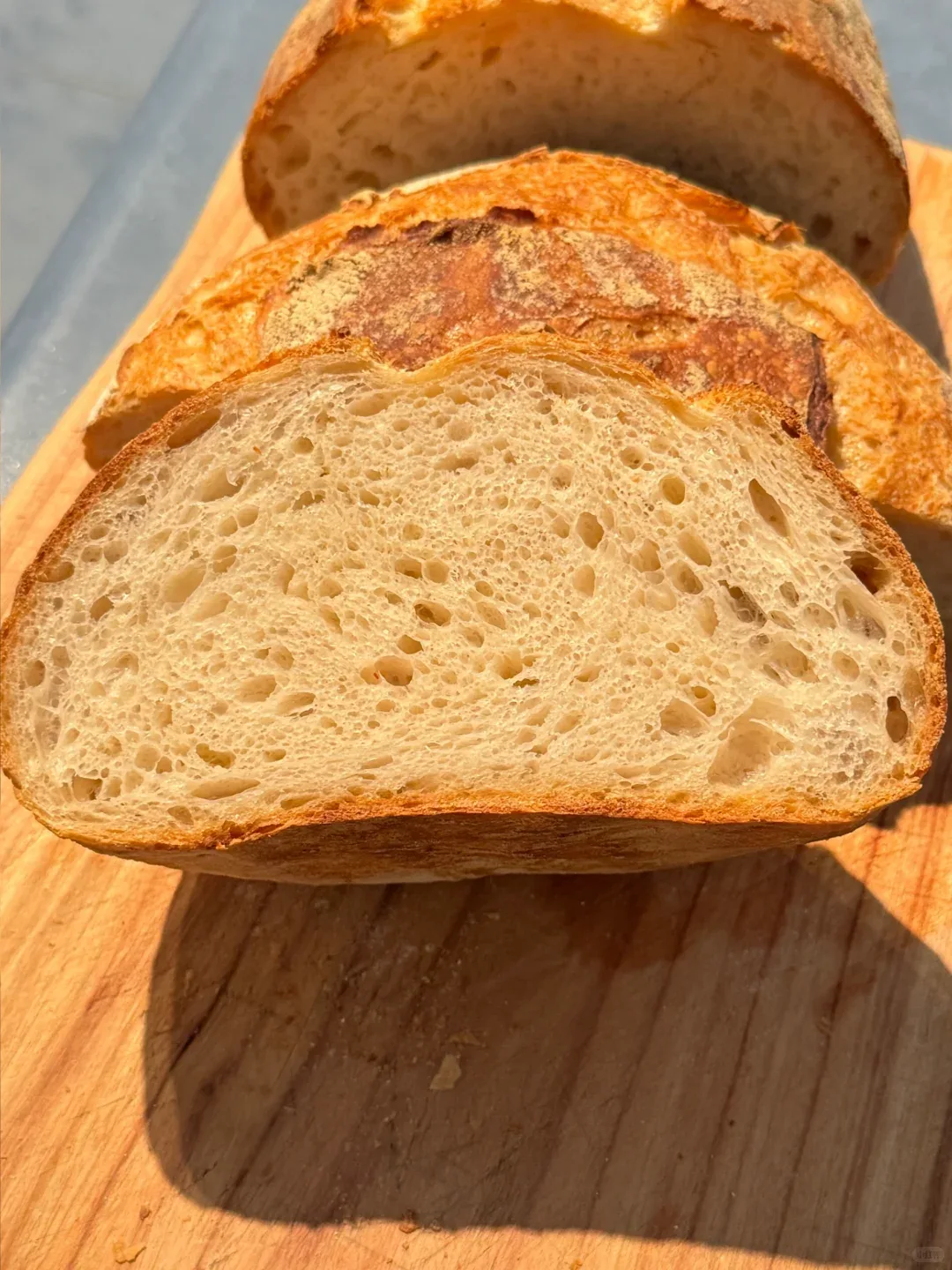 Thick slices of a golden-crusted loaf on a wooden board, showing the soft, even crumb.