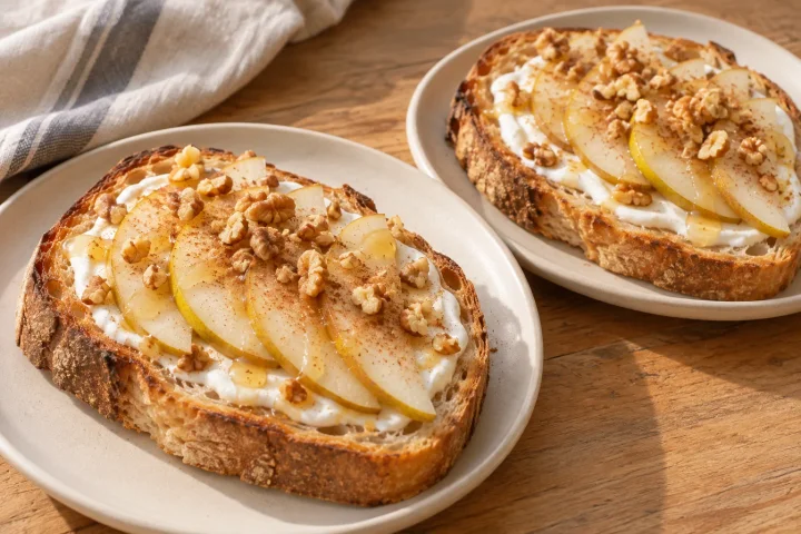 Two natural-crust unseeded sourdough slices topped with white yogurt, fine pear slices, chopped walnuts and a light dusting of cinnamon.