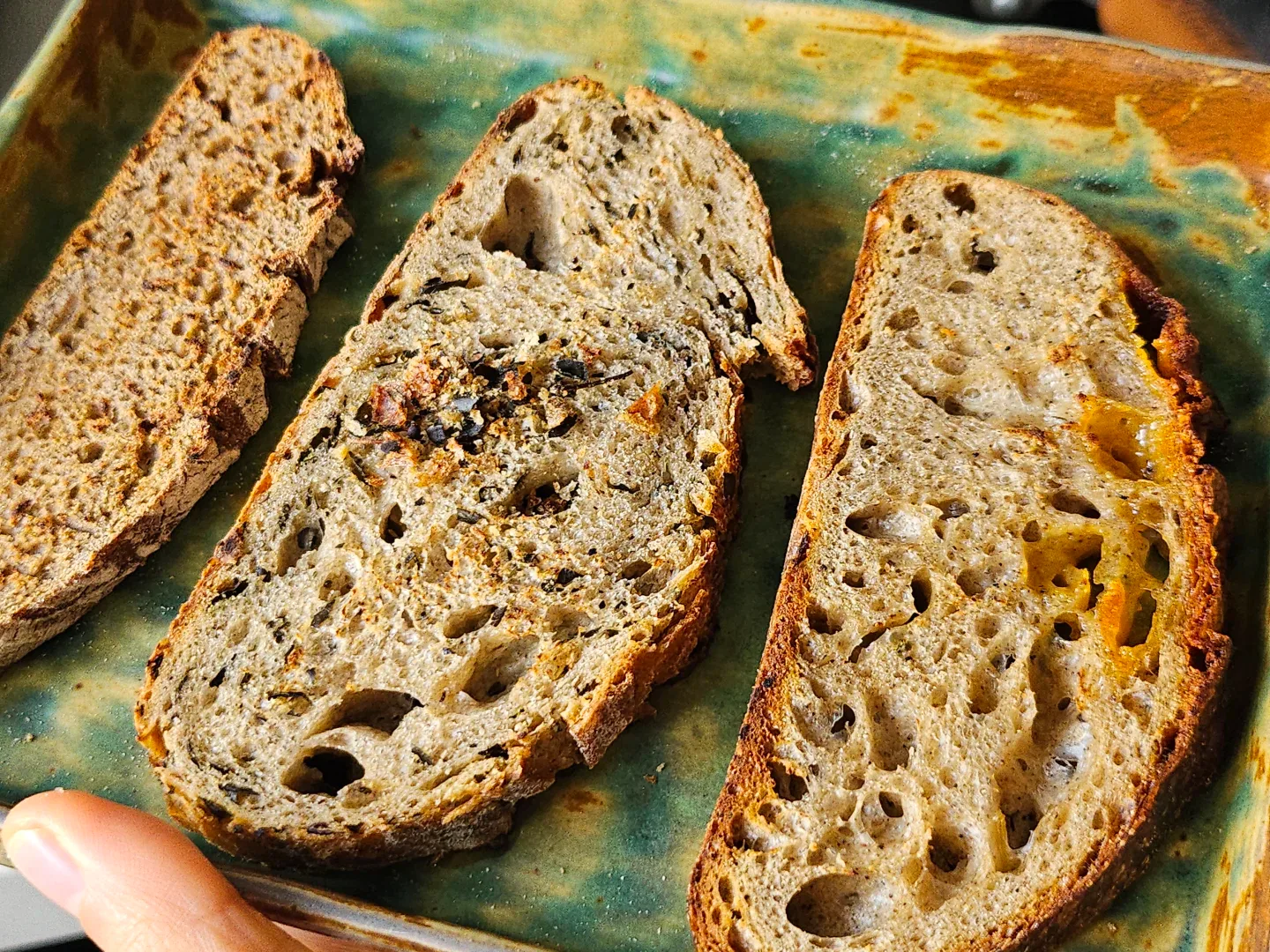 Three different bread slices with textured crumb on a green ceramic platter.